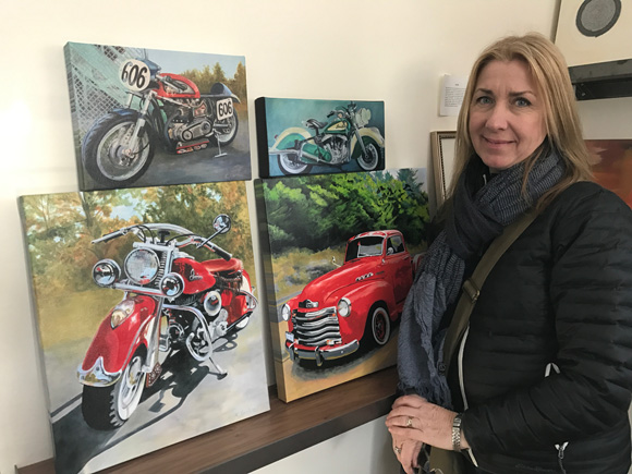 Artist Karen Xarchos pictured with several of her motorcycle and truck prints currently on display at StoryArt.