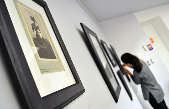 Sarah Allen hangs photographs that show how hat fashions have changed over the years. Photo via the Goulbourn Museum.