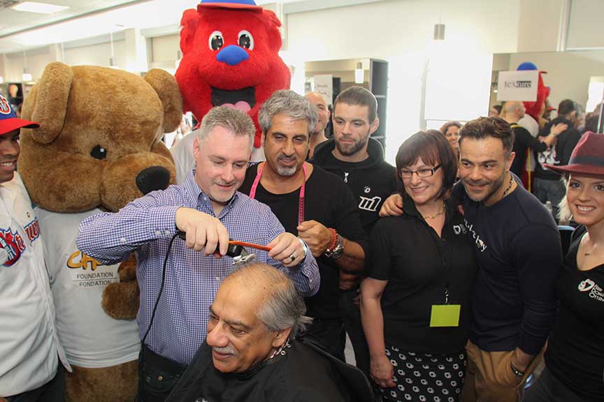 Deputy Mayor Mark Taylor cuts Ward 6 Councillor Shad Qadri at the annual HairDonation Ottawa event at Algonquin College. Looking on are stylist Eli Saikaley and HairDonation Ottawa founder Helen Hutchings (glasses). Barry Gray (StittsvilleCentral)